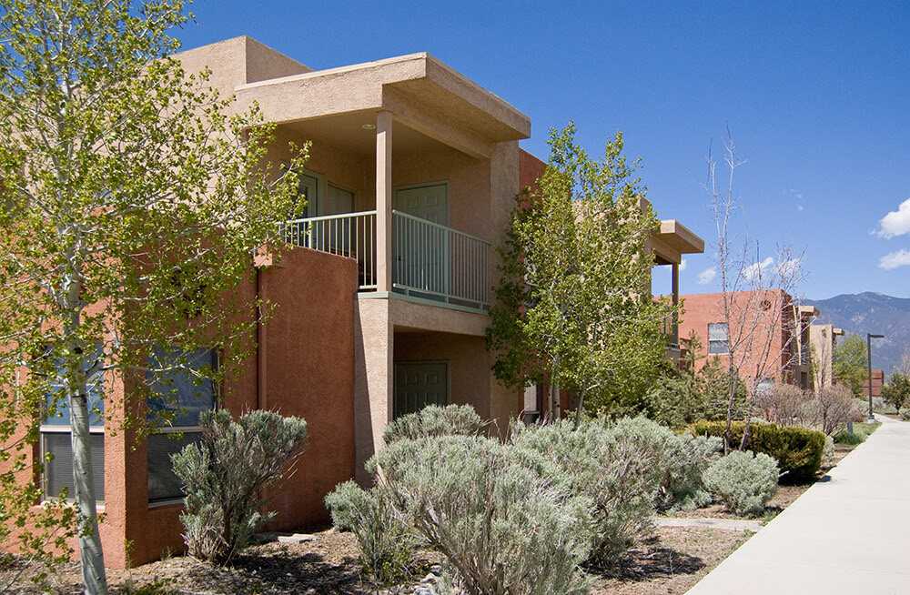 Adobe-toned two-story homes with covered balconies along a sunny walkway at Tierra Montosa, Taos NM