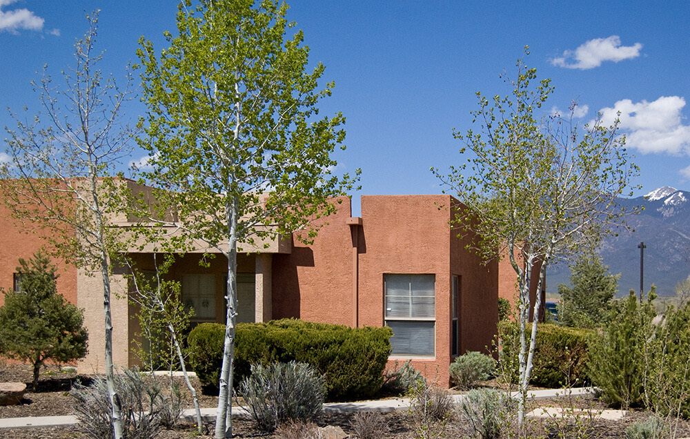 Single-level entrance at Tierra Montosa framed by aspens with mountains behind, Taos NM
