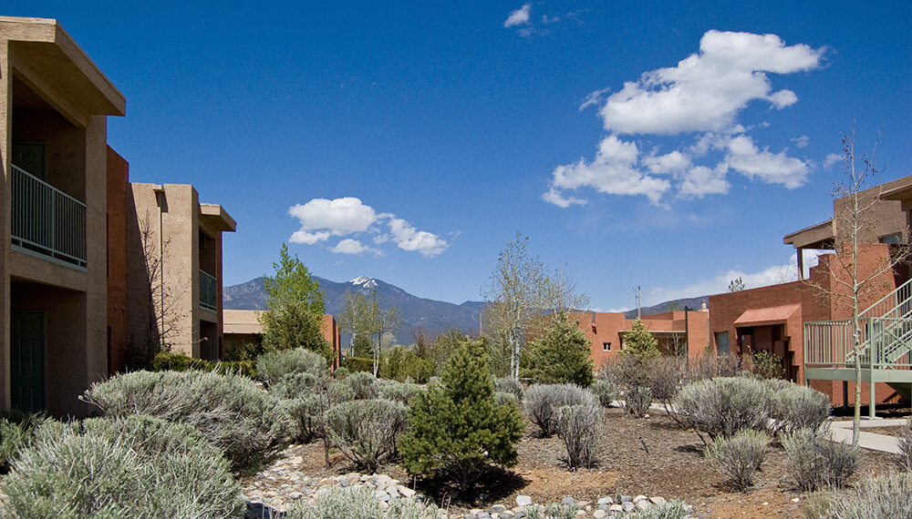 Courtyard of sage, pines, and stone at Tierra Montosa with homes on both sides and Taos Mountain beyond