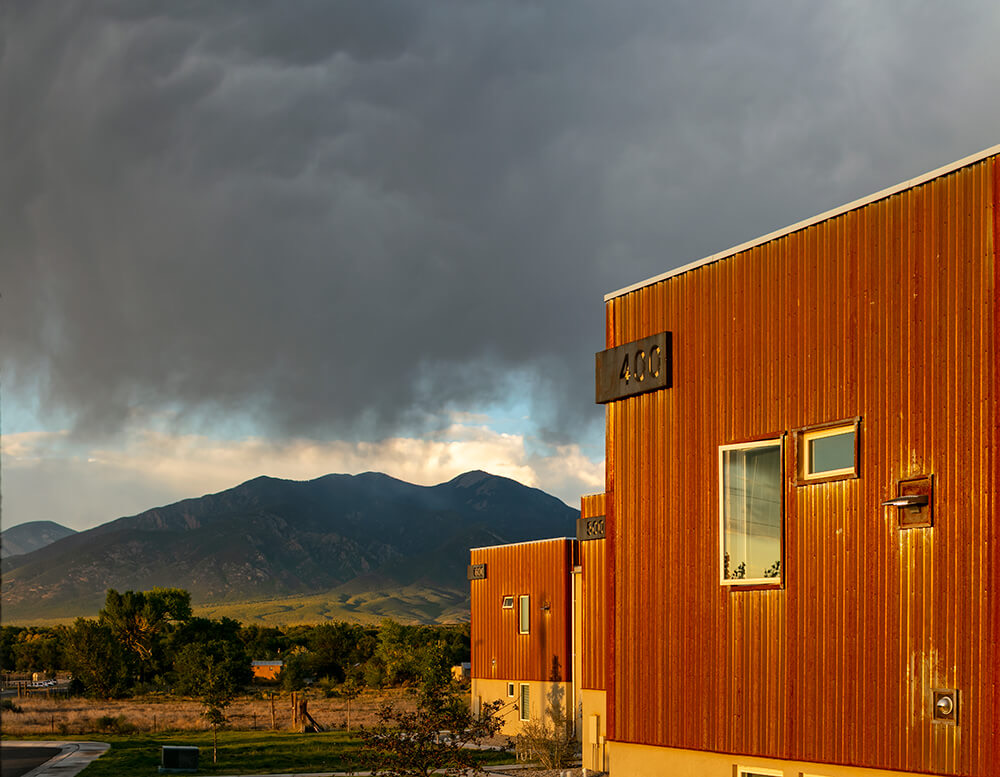 Evening sun on the steel siding of building 400 at Tierra Montosa with a storm over Taos Mountain