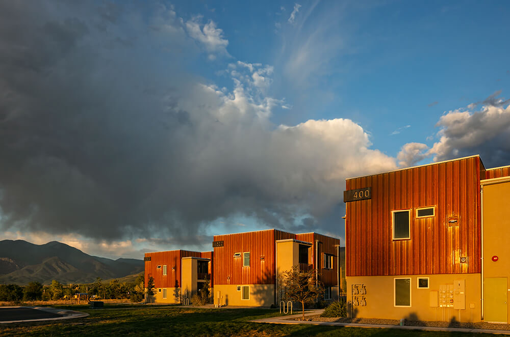 Golden-hour light on three Tierra Montosa buildings with the mountains behind, Taos NM