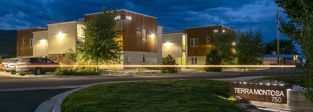 The lit Tierra Montosa entrance sign and homes at nightfall on Gusdorf Road in Taos